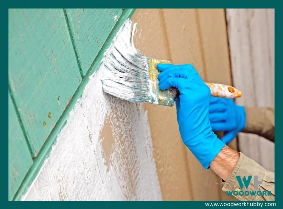 A pair of gloved hands painting a primer on a plywood