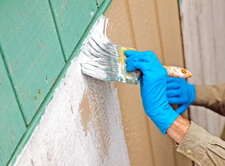 A pair of gloved hands painting a primer on a plywood